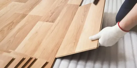 Transform Your Floors with Radiant Resin Inc: Epoxy Coating Calgary 10 Close-up of a hand installing click-lock laminate or luxury vinyl plank (LVP) wood-look flooring over underlayment. Residential flooring and epoxy coating Calgary specialists.