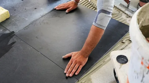 Tile Installation Barrie: Expert Craftsmanship for Beautiful and Lasting Surfaces 9 Tiler's hands pressing down a large black floor tile onto freshly applied mortar.